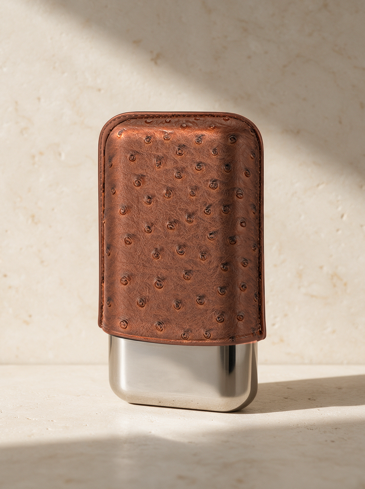 The Cigar Case in Cognac Quill leather with its polished steel cup, on warm stone