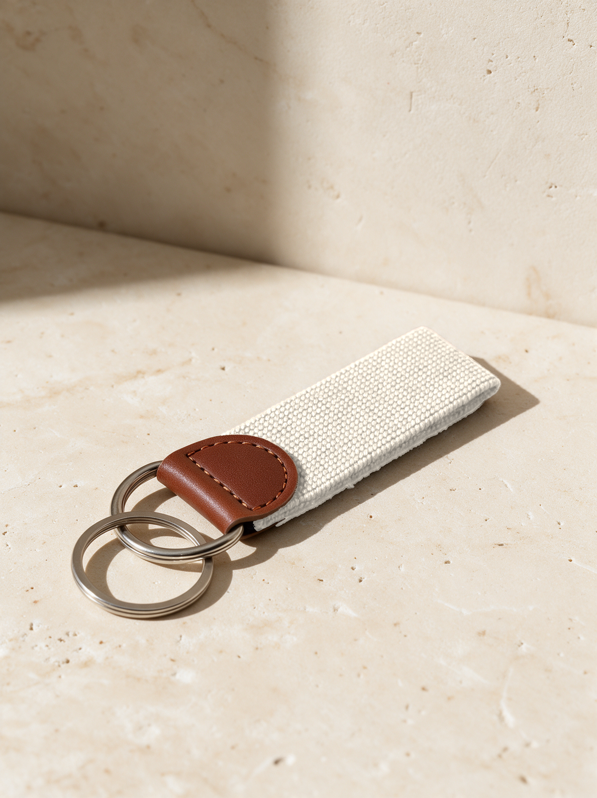 Cream needlepoint key fob with a brown tab on warm stone