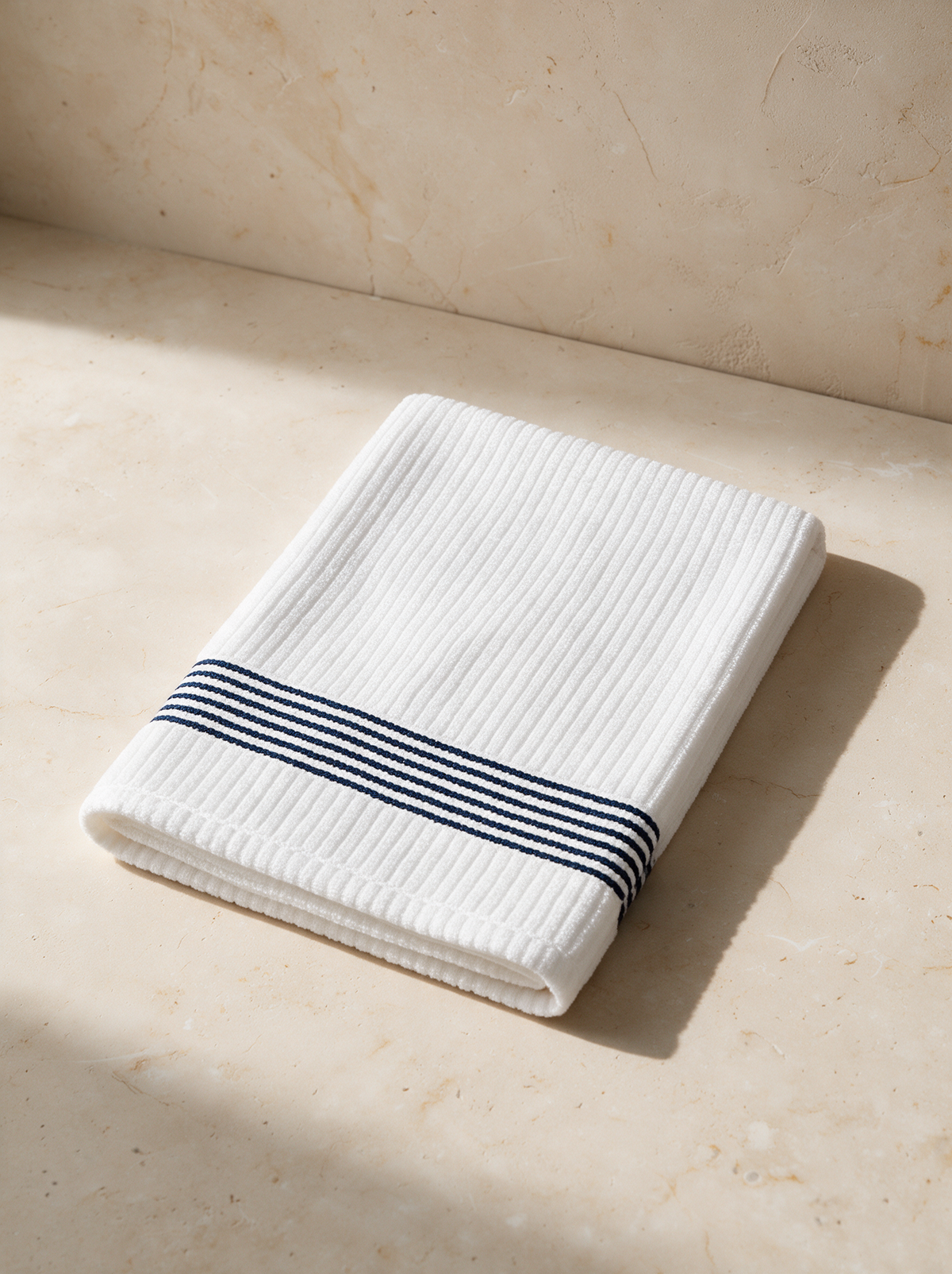 The Golf Towel in white with navy stripes, folded on warm stone