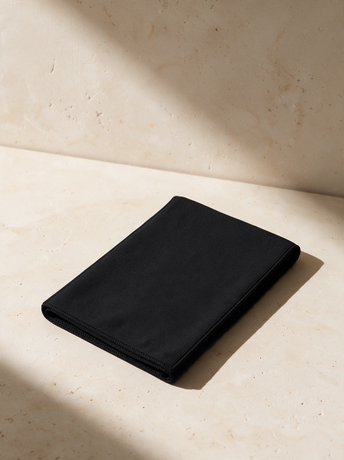 The Sports Towel in black, folded on warm stone